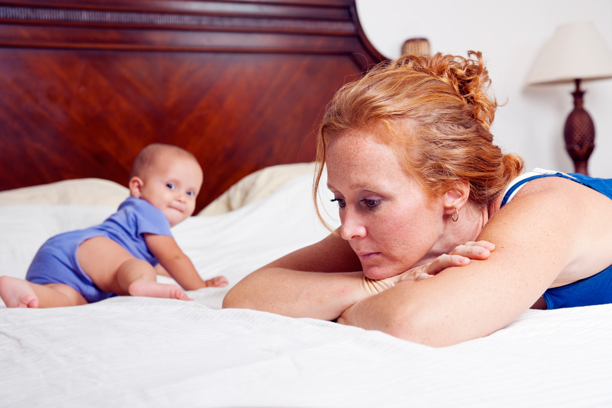 Fehlende Mutterliebe: Frau liegt mit Baby traurig auf dem Bett