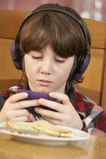 Internetsucht: Junge surft am Esstisch mit dem Smartphone