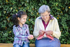 Seniorin bringt Mädchen das Stricken bei.